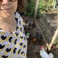 Rosie is wearing a yellow t-shirt with black and white chickens on it, standing in front of three chickens