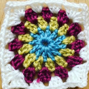 A crochet square, blue centre, yellow and red with a white border ready for a sunburst granny blanket