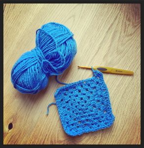 A blue ball of yarn and a granny square