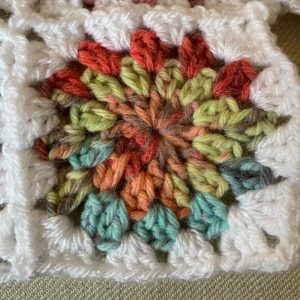 A granny square made with rainbow yarn as part of Rosie's January in blanket form