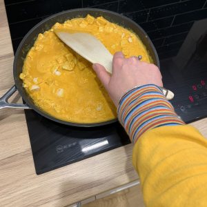 Rosie is stirring her dinner cooking in a pan. The food is the same bright yellow as her sweatshirt