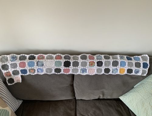 the beginnings of a crochet blanket laid on the back of a sofa