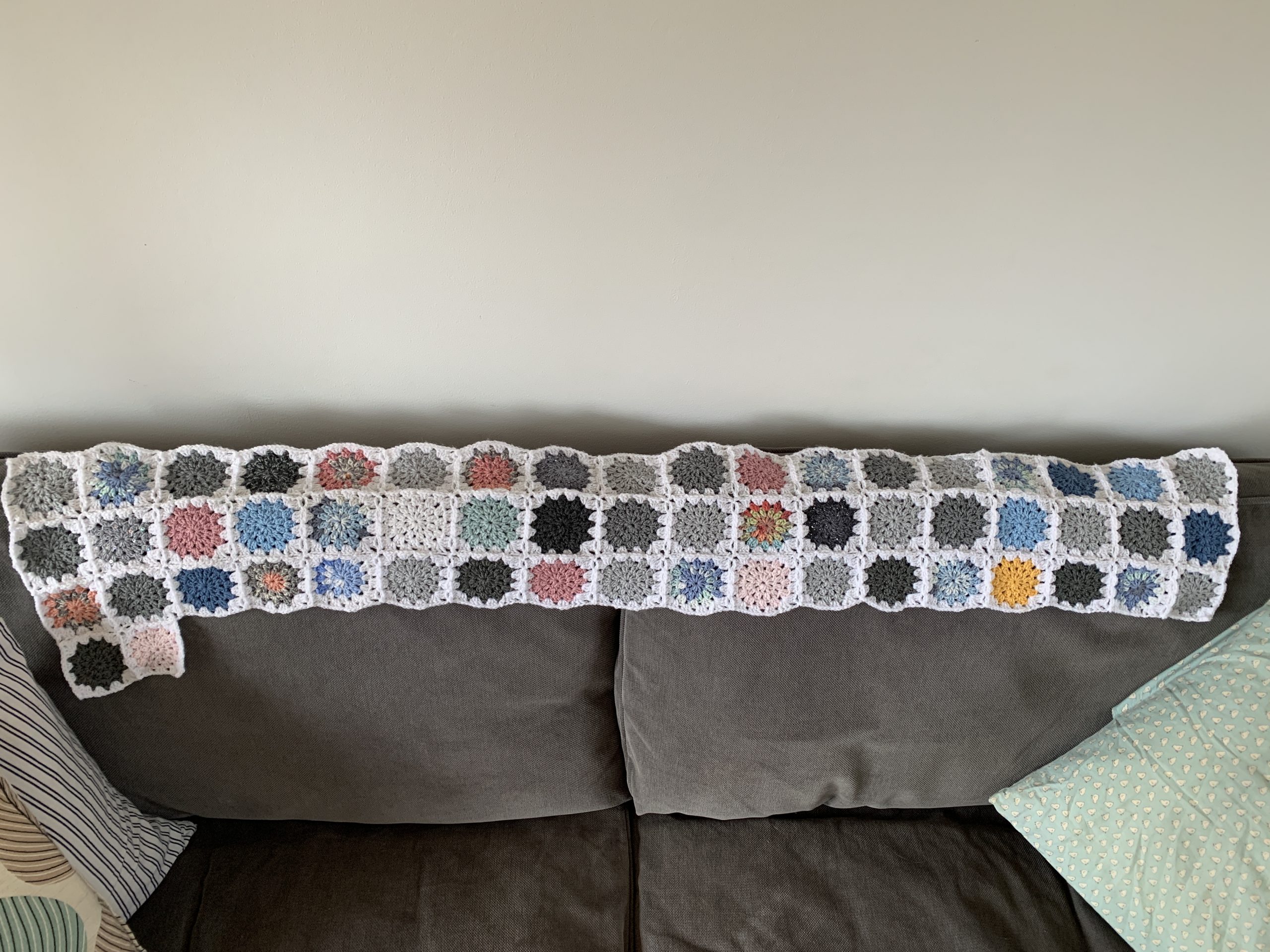 the beginnings of a crochet blanket laid on the back of a sofa