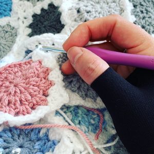 A hand wearing a splint, crocheting a granny blanket