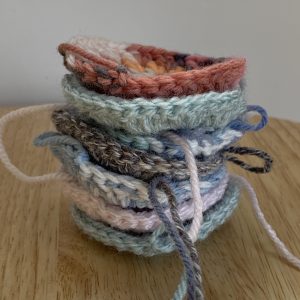 A stack of crochet circles in shades of grey, blue and pink, ready to be added for Rosie's sky blanket April update