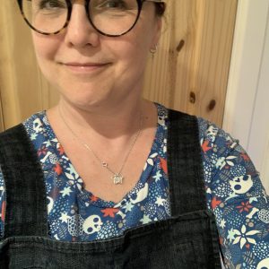 A white woman wearing a denim pinafore and a blue long sleeved t-shirt with skulls and flowers on it (Me Made May 2021 week three)