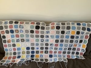 A granny square blanket made up of squares in shades of grey, blue, pink, yellow and white to represent the sky. 